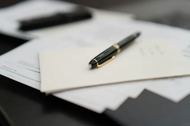 Una ploma estilogràfica damunt d'un sobre i uns papers.