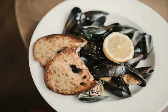 Un plat de musclos amb pa torrat i una rodanxa de llimona.